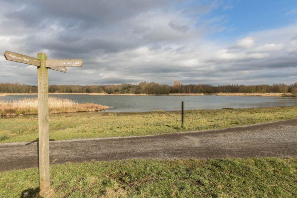 A wooden signpost pointing towards a large lake with woodland in the distance